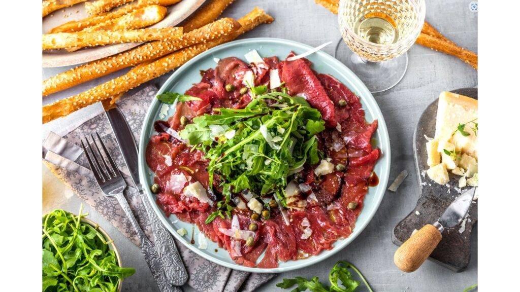 Carpaccio di Manzo je elegantná talianska delikatesa, ktorá sa skladá z veľmi tenko nakrájaného surového hovädzieho mäsa, zvyčajne sviečkovice. Táto lahôdka je známa svojou jemnou chuťou a jemnou textúrou, ktorá sa dosahuje len kvalitným a čerstvým mäsom. Carpaccio sa tradične podáva s olivovým olejom, citrónovou šťavou, parmezánom, rukolou a niekedy aj s kaparami, čím vzniká osviežujúca a vyvážená chuťová kombinácia.